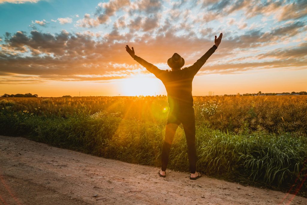 Person on a gravel path facing the sunset with their arms outstretched