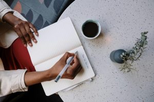 Person writing in a journal with a cup of coffee.