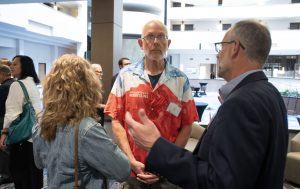 Three adults stand together talking. One is wearing a shirt printed with a image of a mountain and the words "Minds Over Mountains."