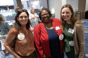 Three adult people stand together. They are wearing blazers and dress shirts and some are wearing a button that reads "Ask me about alzheimers research."
