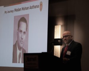 A man stands at a podium holding a microphone and gesturing. A screen behind him reads alzheimers ends here.