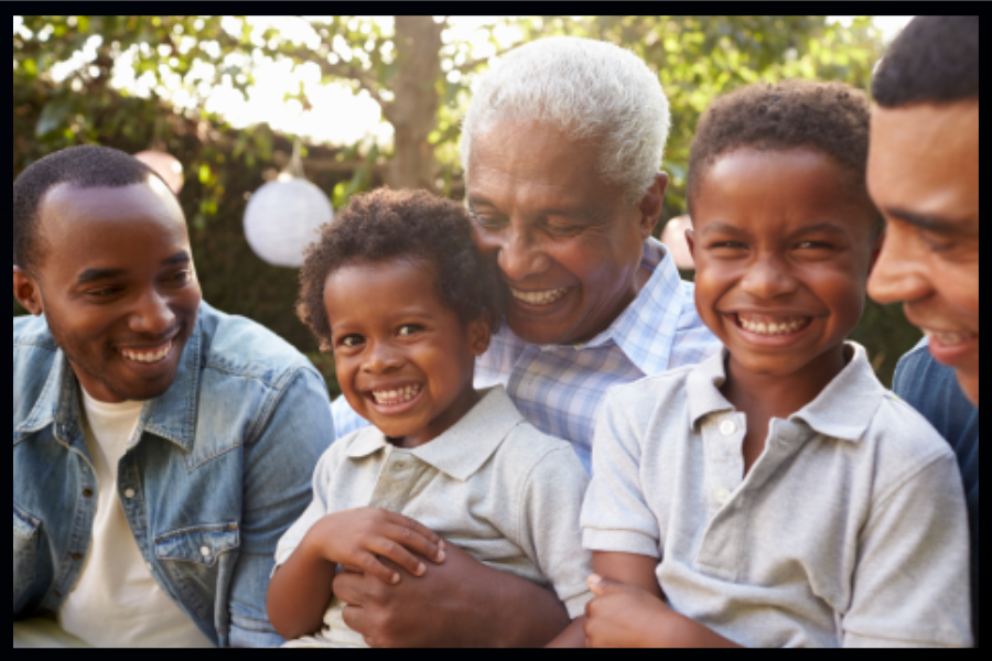 Two adults and two children laughing together outside on a bright day.